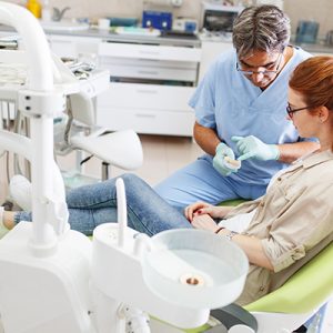 older-male-dentist-speaking-to-female-patient-in-dental-office